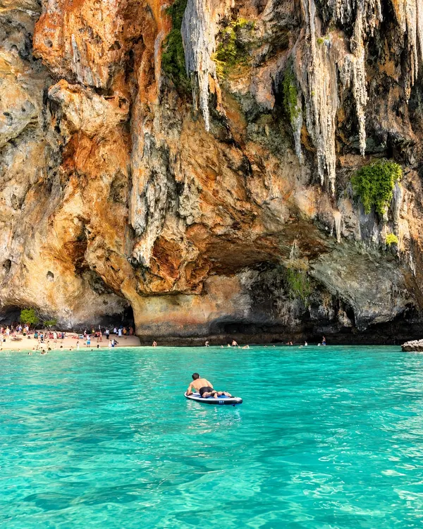 Guest on a paddleboard in turquoise water below the limestone cliffs at Phra Nang Cave, Railay
