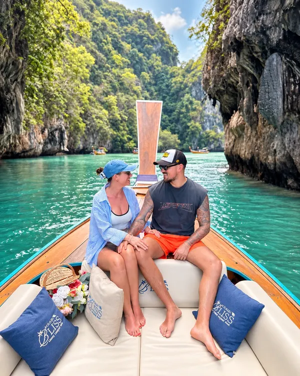 Couple sitting on the bow of the longtail boat in a narrow channel between limestone cliffs