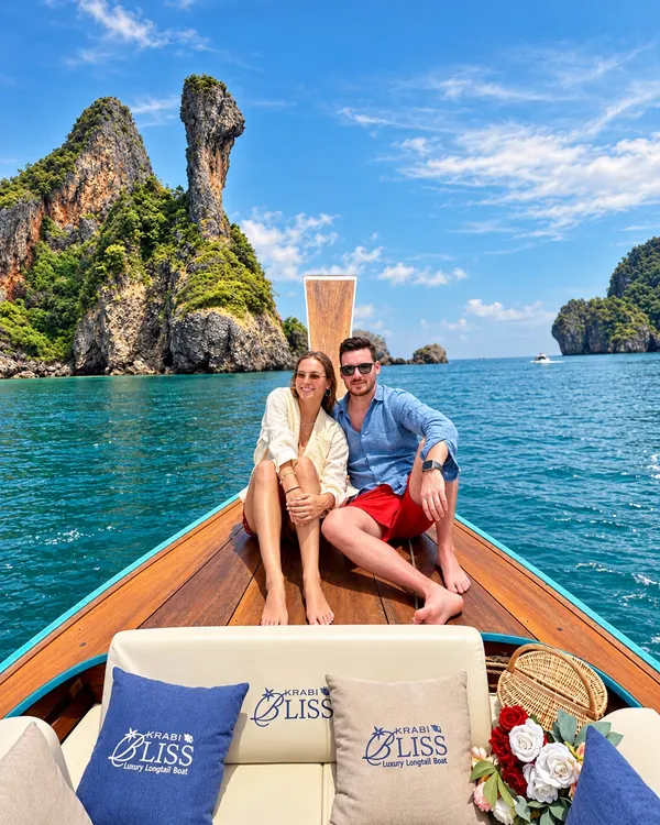 Couple sitting on the bow of the longtail boat with Chicken Island behind
