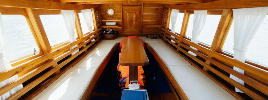 Shaded cabin of the Krabi Bliss longtail boat, with cushioned benches, a wooden table and life jackets stowed underneath