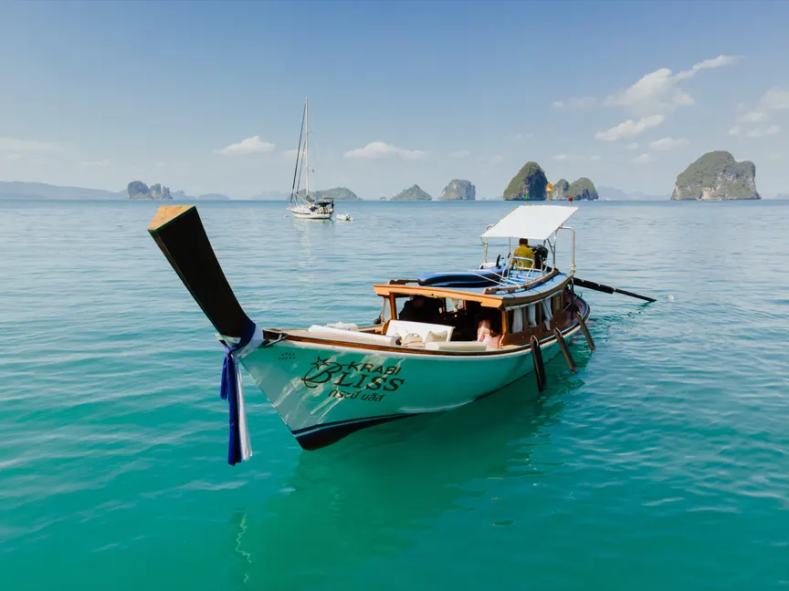 The Krabi Bliss private longtail boat on the water off Krabi, with the boat's name on the hull and limestone islands behind